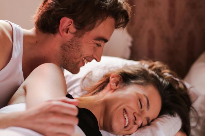 A joyful couple enjoying a cozy morning in bed with sunlight streaming in.