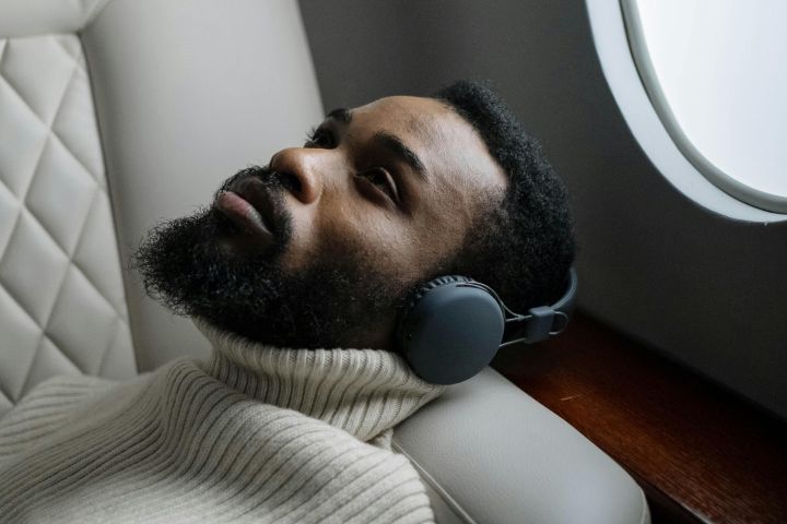 Man reclining on an airplane seat, wearing wireless headphones and a sweater, looking relaxed.