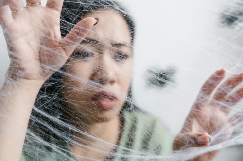 Close-up of a woman looking trapped behind a spider web, conveying anxiety.