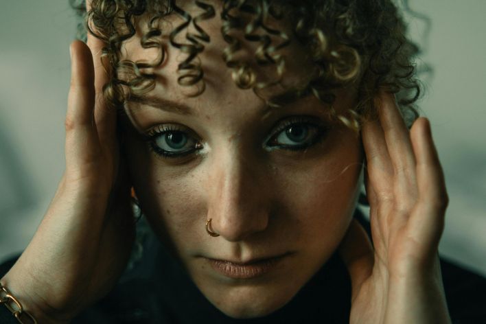 Close-up portrait of a woman with curly hair and nose ring expressing emotion and introspection.