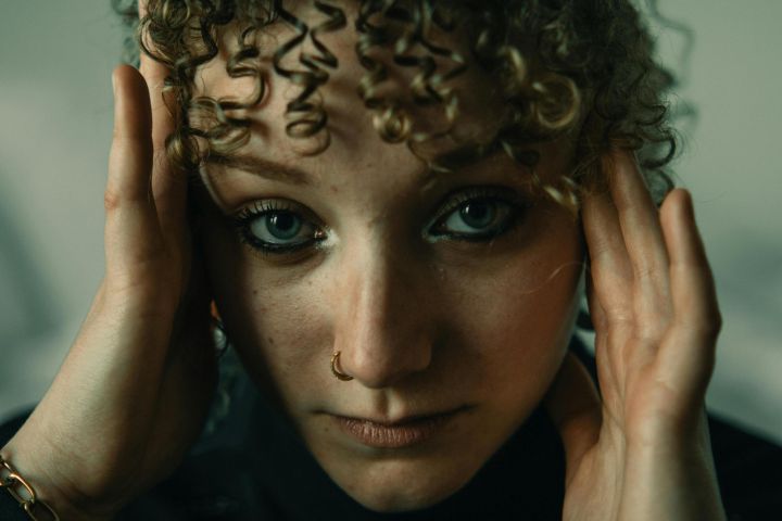 Close-up portrait of a woman with curly hair and nose ring expressing emotion and introspection.