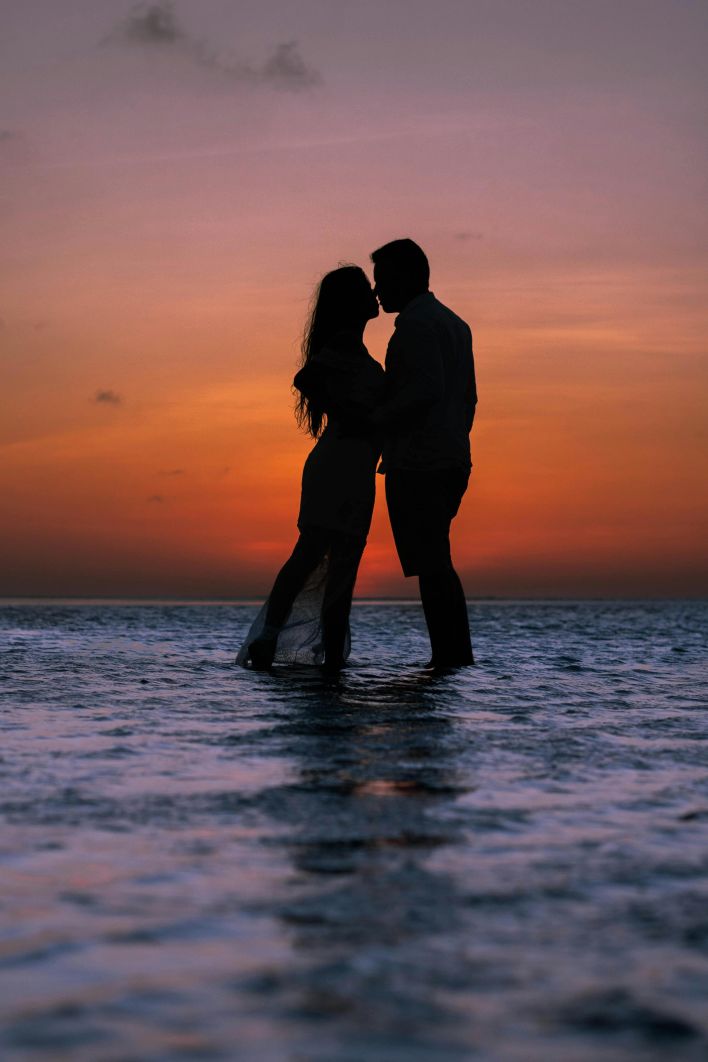 Silhouette of a couple kissing at the beach during a vibrant sunset, creating a romantic ambiance.
